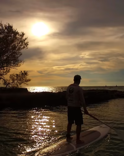 Remador en paddle board al atardecer, con el sol entre nubes sobre el mar Caribe