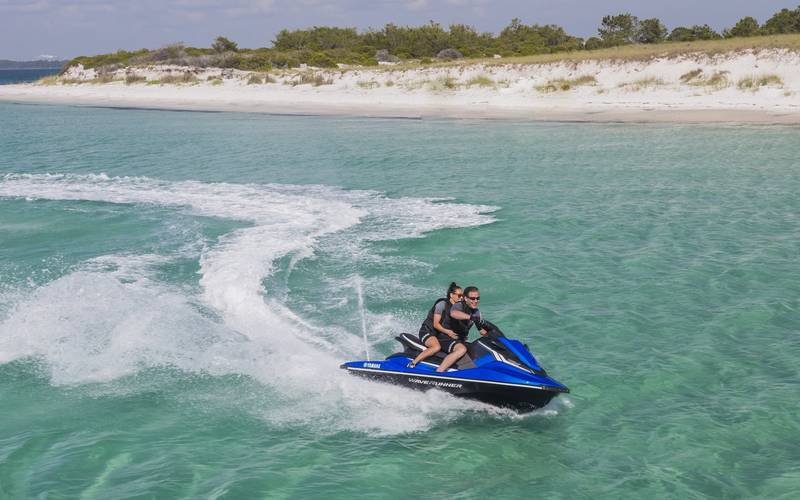 Dos personas en un jet ski Yamaha sobre agua turquesa frente a una playa de arena blanca cerca de Cartagena