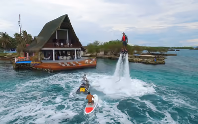 Piloto de flyboard sobre chorros de agua junto a una moto acuática, en aguas turquesa de las islas