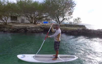 Remador sobre un paddle board blanco en aguas verde turquesa junto a una isla