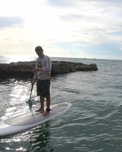 Remador de Colombia Flyboard de pie sobre un paddle board, acercándose por aguas verde turquesa junto a una isla